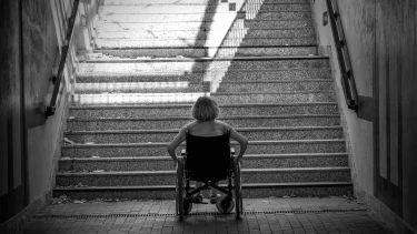 En dame i en kørestol foran nogle trapper hun ikke kan komme op ad