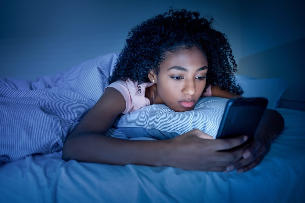 Pige kigger på telefon mens hun ligger i sin seng