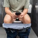 Mand scroller på sin telefon, mens han sidder på toilettet