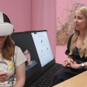 Kvinde sidder med VR-briller på mens terapeut viser en avatar af en fiktiv stemmehallucination på en computerskærm