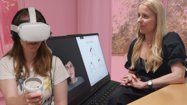 Kvinde sidder med VR-briller på mens terapeut viser en avatar af en fiktiv stemmehallucination på en computerskærm