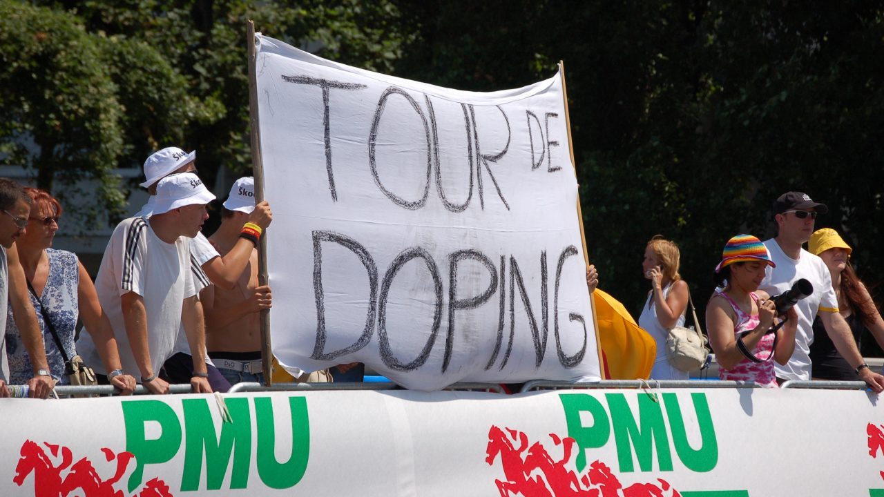 Unge mænd der til tour de france holder et bander med ordene 'tour de doping'