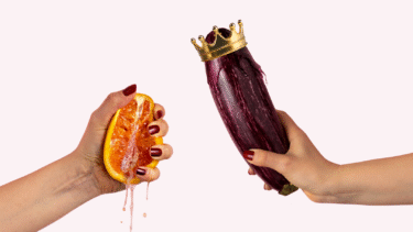 En hånd med røde negle presser en saftig appelsin, mens en anden hånd holder en aubergine med en guldkrone. Baggrunden er lyserød.