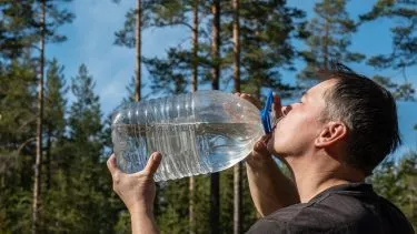Man drikker vand af store flaske i skoven