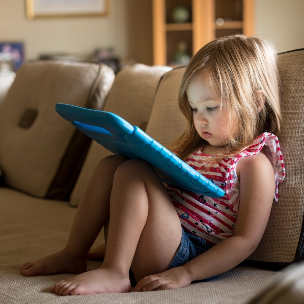 Lille pige sidder i sofa med tablet