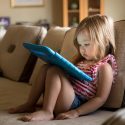 Lille pige sidder i sofa med tablet