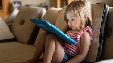 Lille pige sidder i sofa med tablet