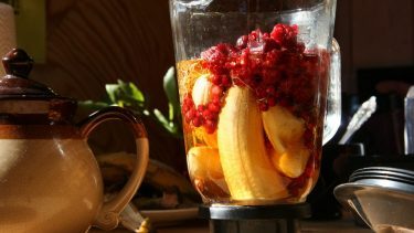 En blender på et køkkenbord, som er fyldt med lækre ingredienser, men blenderen har endnu ikke lavet frugten (inklusiv en banan) og bærerne til en smoothie.