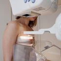 Yngre kvinde får mammografi af højre bryst, man ser ikke hendes ansigt, det er bag maskinen