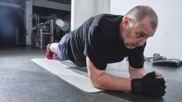 Mand med gråt hår laver planken i fitness centeret