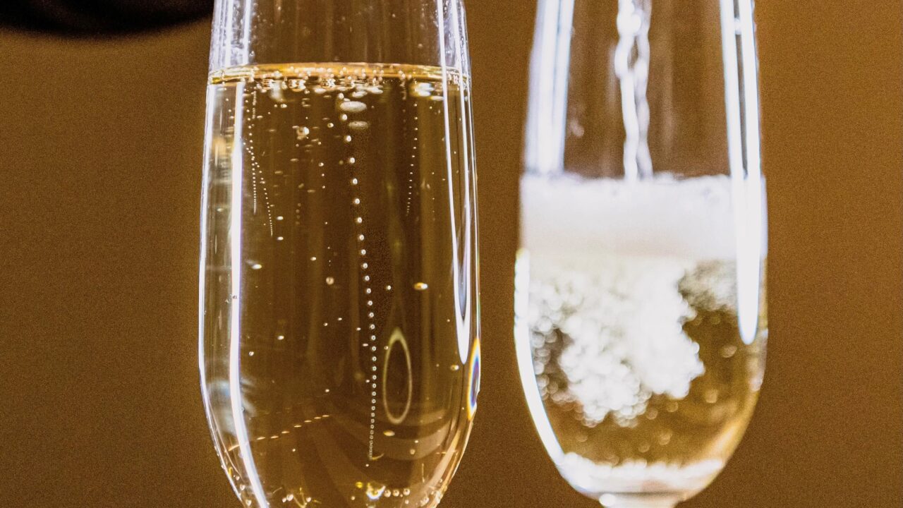 Champagne skænkes i glas og bobler stiger i kæde