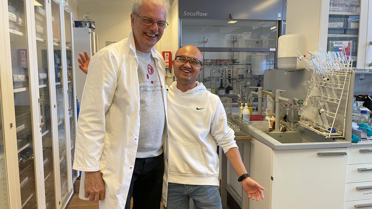 Morten Meldahl står i laboratoriet iført hvid kittel sammen med ph.d.-studerende, Yuan Zhang
