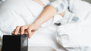 person trykker på snooze knappen fra sengen