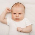 Baby ligger på ryggen med rynket pande