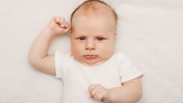 Baby ligger på ryggen med rynket pande
