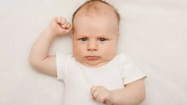 Baby ligger på ryggen med rynket pande
