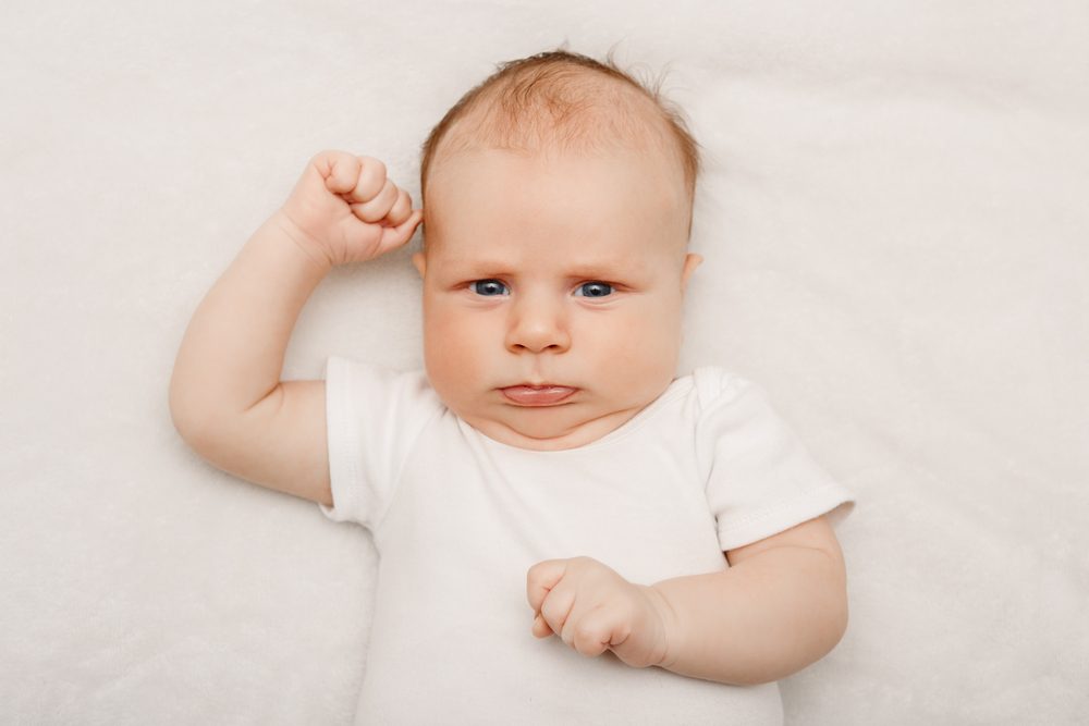 Baby ligger på ryggen med rynket pande