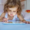 Lille pige, omkring 3-4 år, ligger på maven og spiller på sin tablet