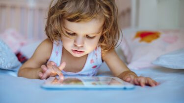 Lille pige, omkring 3-4 år, ligger på maven og spiller på sin tablet