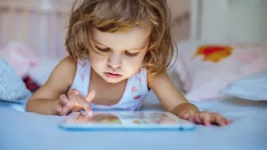 Lille pige, omkring 3-4 år, ligger på maven og spiller på sin tablet