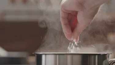 Hånd hælder salt i gryde