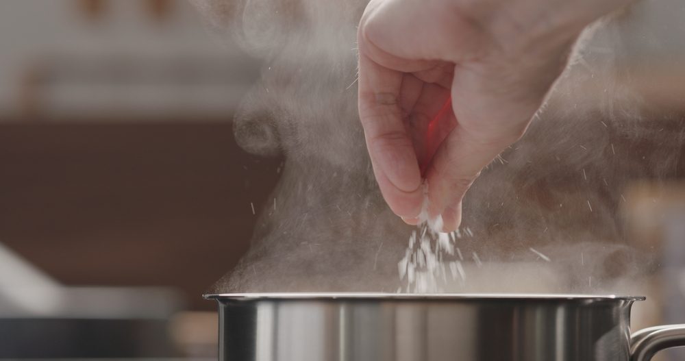 Hånd hælder salt i gryde