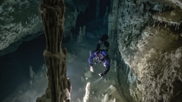 En dykker i en blå dykkerdragt svømmer ind i mellem en underjordisk grotte