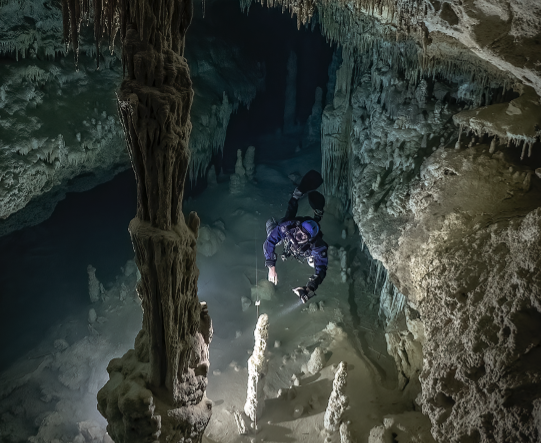 En dykker i en blå dykkerdragt svømmer ind i mellem en underjordisk grotte