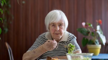 Ældre kvinde med gråt hår spiser middag alene i en havestue