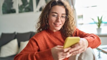 ung-kvinde-med-briller-og-krøller-kigger-på-sin-smartphone