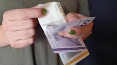 Kvindehænder bladrer mellem dansk 100-kroneseddel og halvtredskroneseddel