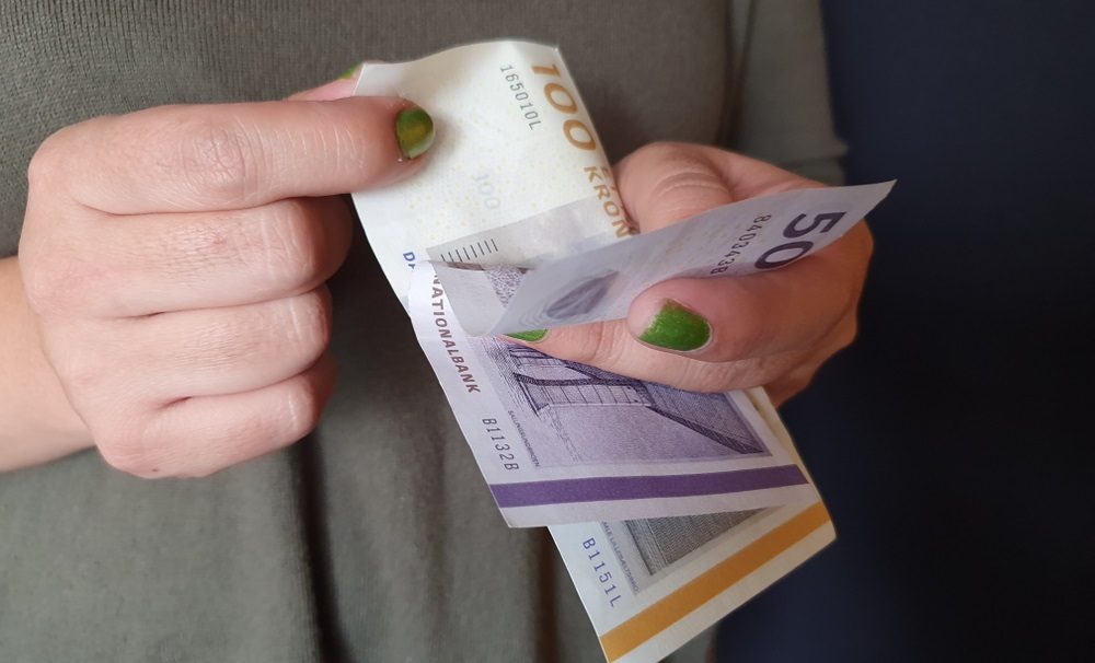 Kvindehænder bladrer mellem dansk 100-kroneseddel og halvtredskroneseddel