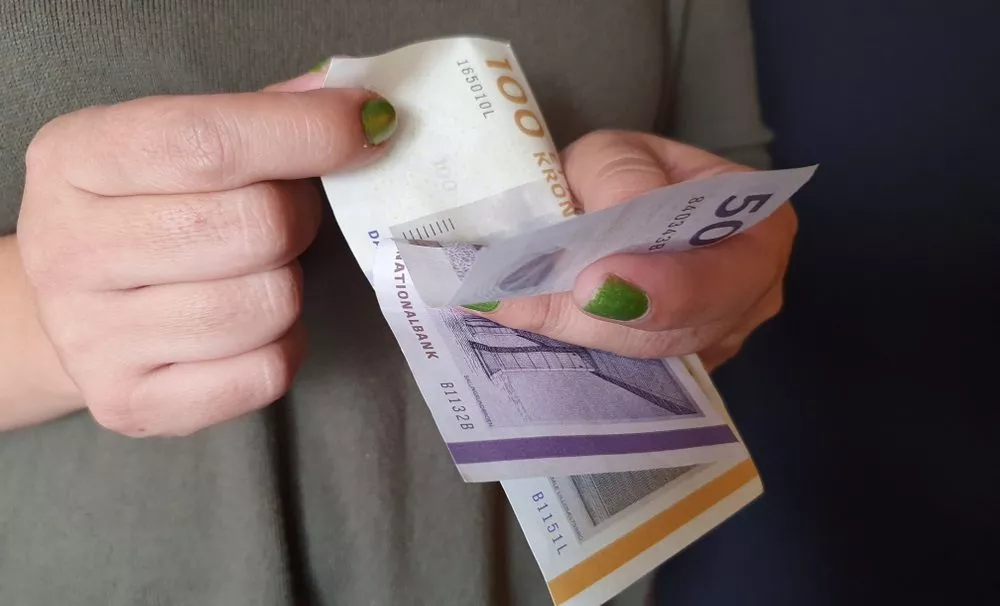 Kvindehænder bladrer mellem dansk 100-kroneseddel og halvtredskroneseddel