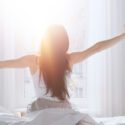 Mørkhåret kvinde, der trækker gardin fra om morgenen, hvor solen stråler ind