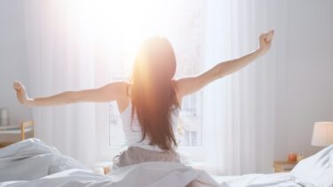 Mørkhåret kvinde, der trækker gardin fra om morgenen, hvor solen stråler ind