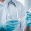 Læge med blå handsker holder en sprøjte med en vaccine