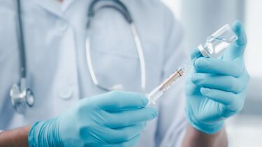 Læge med blå handsker holder en sprøjte med en vaccine