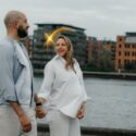 Foto af en gravid kvinde og hendes mandlige partner, der holder i hånden langs Islandsbrygge havnefront.