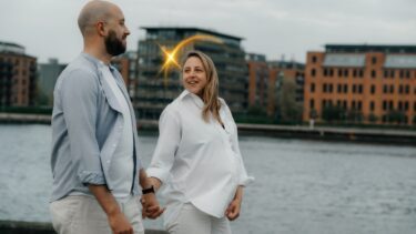 Foto af en gravid kvinde og hendes mandlige partner, der holder i hånden langs Islandsbrygge havnefront.