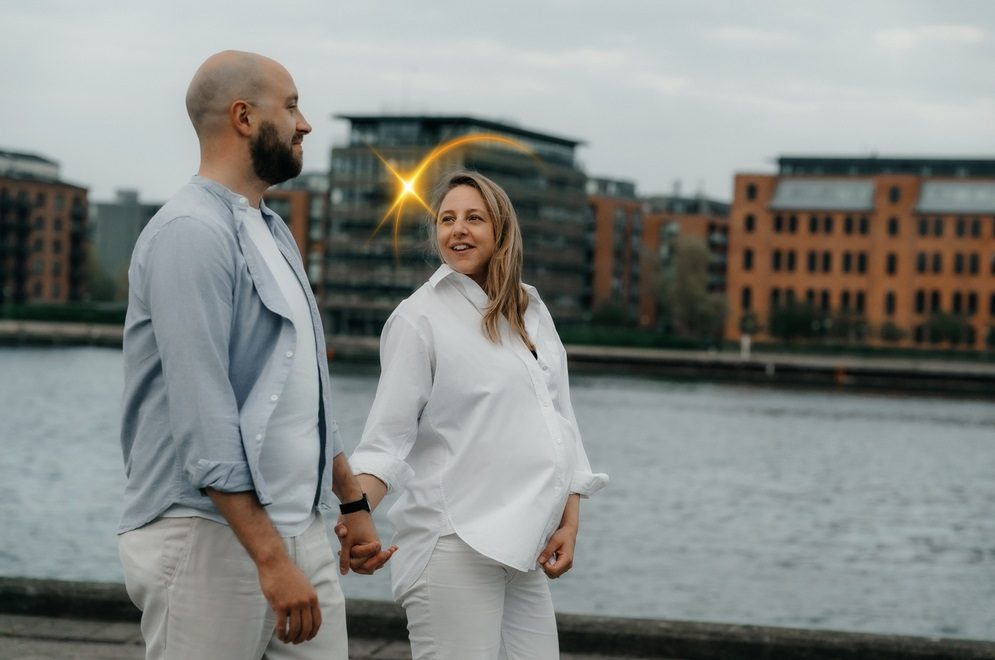 Foto af en gravid kvinde og hendes mandlige partner, der holder i hånden langs Islandsbrygge havnefront.