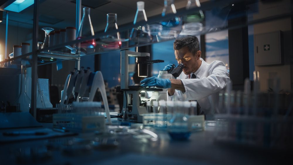 Mand kigger i mikroskop på laboratorium.