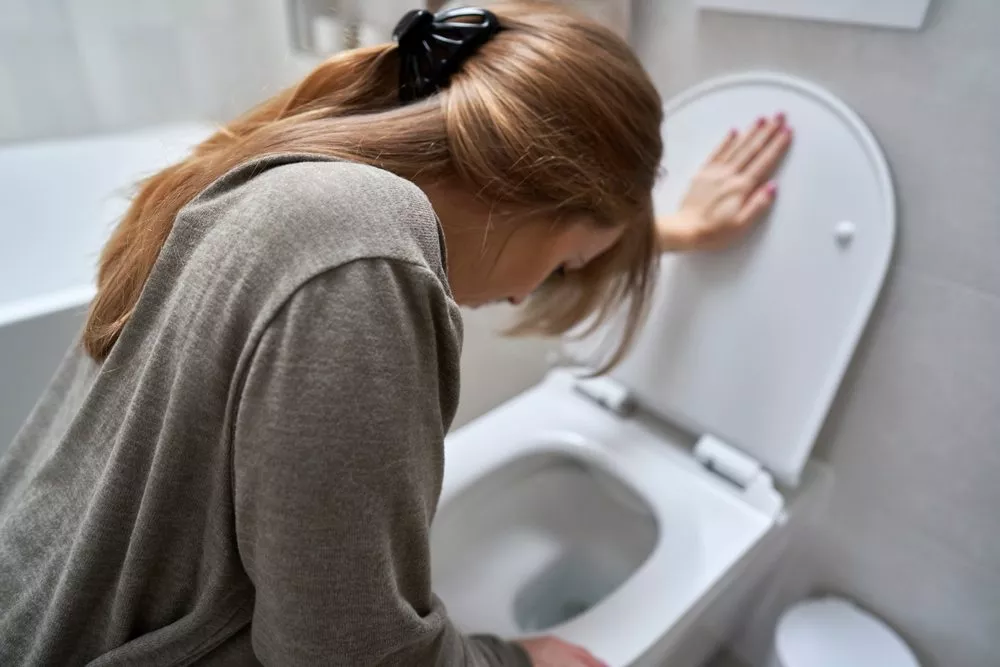 Foto af kvinde, der sidder bøjet over toiletkummen.