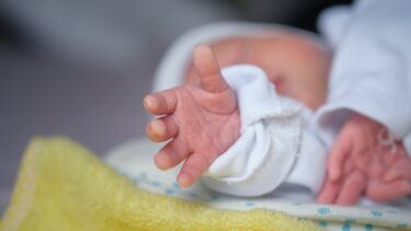 En nyfødt baby rækker ud efter beskueren.