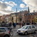 Biler kører ved Christianshavn i København, mens fodgængere venter ved en fodgængerovergang.