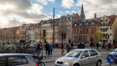 Biler kører ved Christianshavn i København, mens fodgængere venter ved en fodgængerovergang.