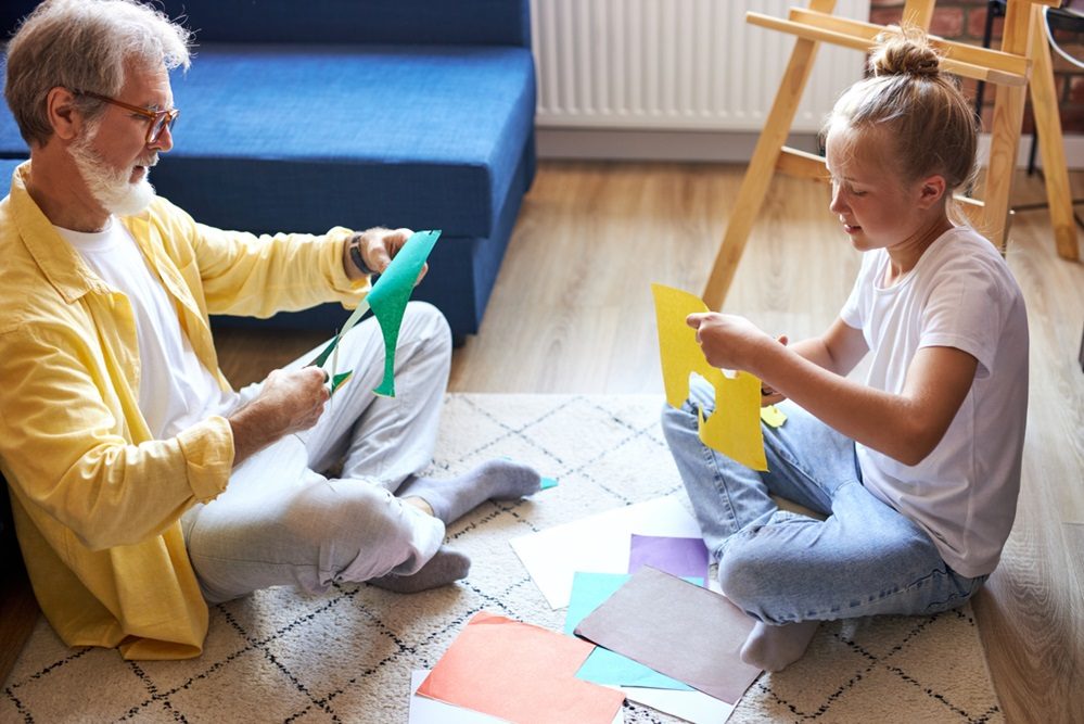 Billede af en mand og et barn, der laver papirklip på gulvet.