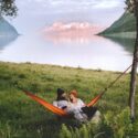 Foto af et par, der sidder i en hængekøje sammen og ser glade ud med smuk natur i baggrunden.