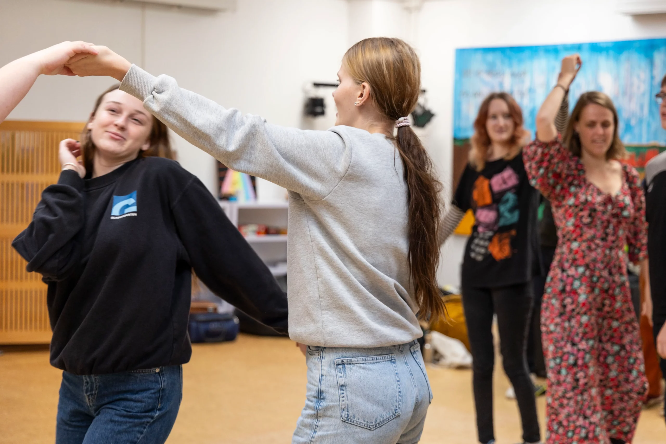 Piger danser i en gymnastiksal. En pige danser under en bro af armen, der holdes udstrakt over hende