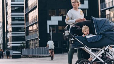 Kvinde er på tur i varmt efterårsvejr med sin baby i en barnevogn i københavnske byomgivelser.