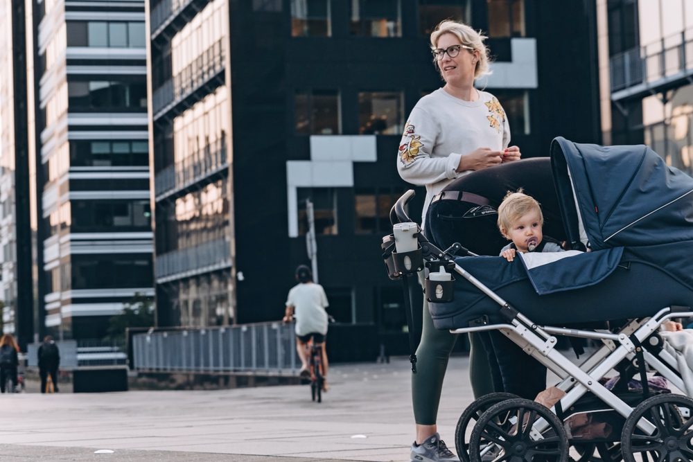 Kvinde er på tur i varmt efterårsvejr med sin baby i en barnevogn i københavnske byomgivelser.